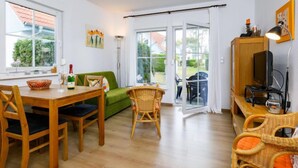 A modern living room with a wooden dining table, green sofa, wicker chairs, and a television on a wooden stand. - Apartment Jacobs by Interhome (Zinnowitz)
