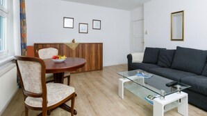 Un salon moderne avec une table ronde en bois, deux fauteuils rembourrés, un canapé gris foncé et une table basse en verre.