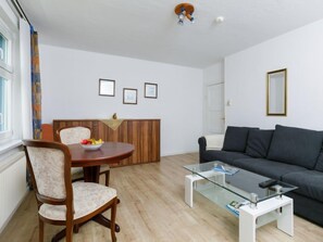 Ein modernes Wohnzimmer mit einem runden Holztisch, zwei Polstersesseln, einem dunkelgrauen Sofa und einem Glastisch.