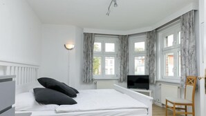 Une chambre à coucher avec un lit, une télévision, une chaise et une fenêtre avec des rideaux.