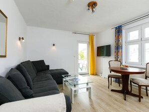 Ein modernes Wohnzimmer mit einer schwarzen Couch, einem Glastisch und einem Holzesstisch mit Stühlen.