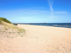 Uma praia arenosa com céu claro e um cais ao longe.
