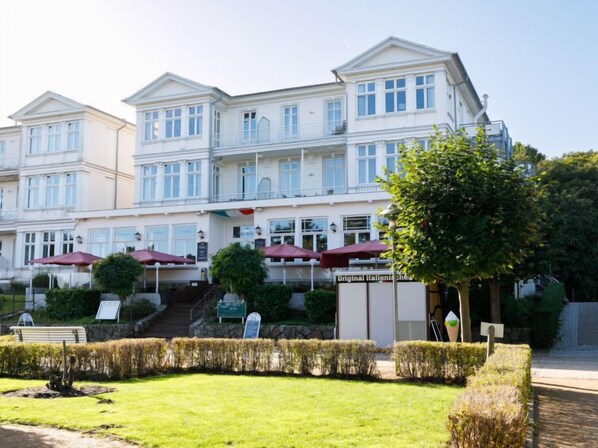 A multi-story hotel with a classic architectural style, featuring a central entrance with steps, outdoor seating with umbrellas, and well-maintained landscaping. - App.13 Zinnowitzer Hof by Interhome (Zinnowitz)