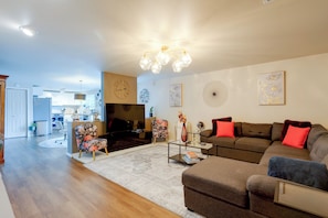 Ein modernes Wohnzimmer mit Sofa, Sessel und Couchtisch. Ein Fernseher, eine Uhr und Wanddekoration sind ebenfalls vorhanden.