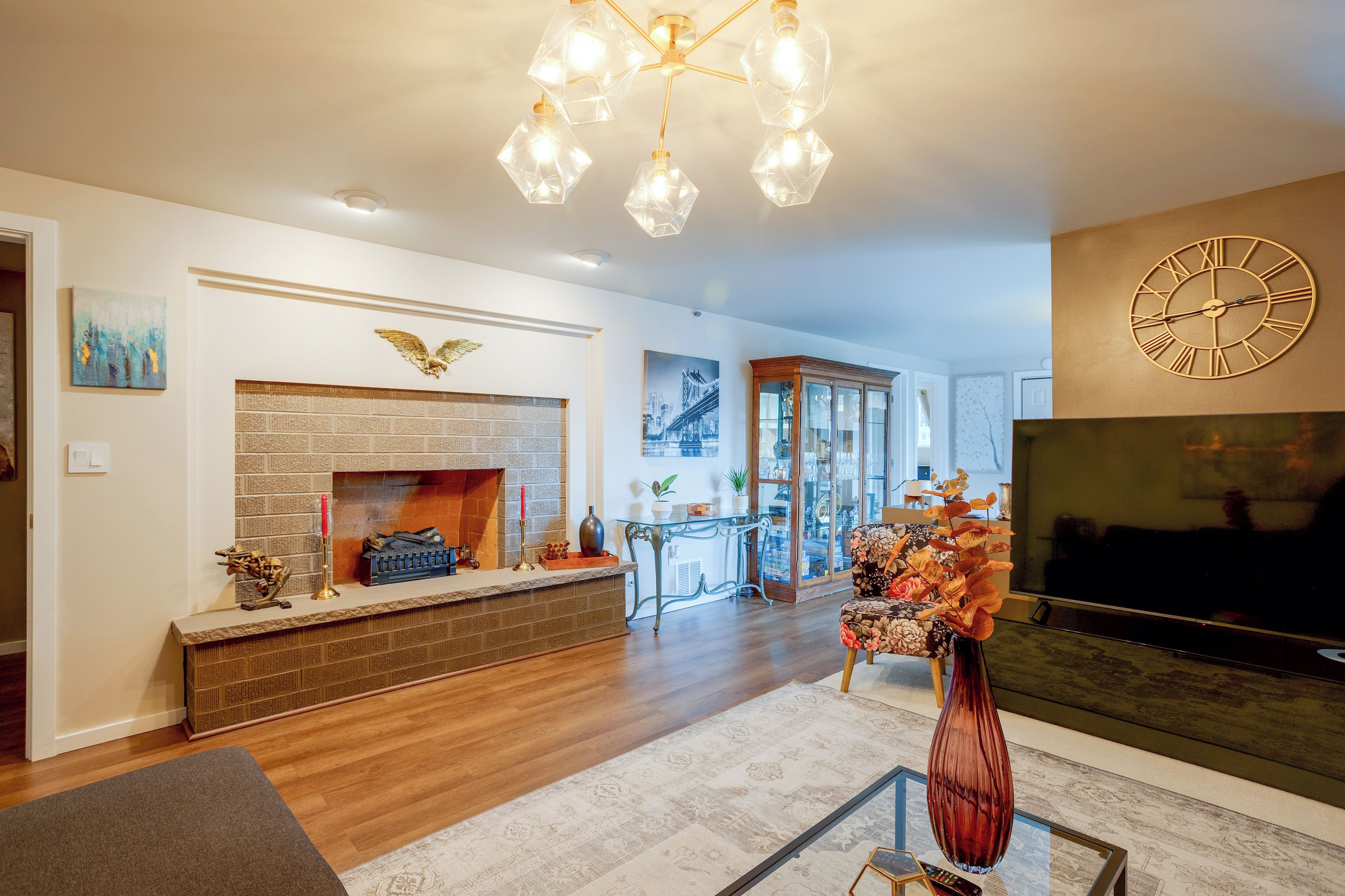 A living room with a fireplace, a large clock, and a television.