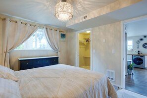 Ein Schlafzimmer mit Bett, einem Fenster mit Vorhängen, einem Nachttisch und einer Tür zu einem Badezimmer.