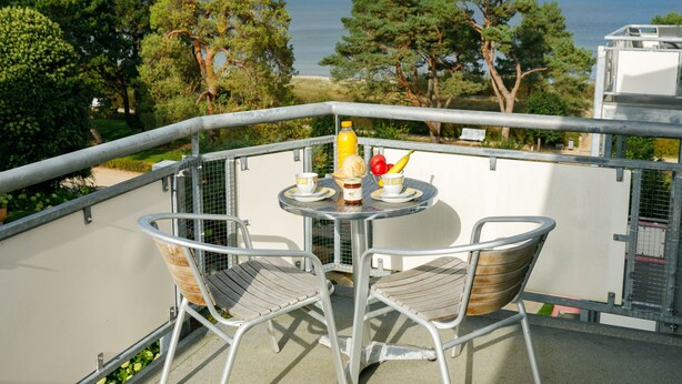 A balcony with a table and chairs, overlooking a beach and trees. - App.17 Zinnowitzer Hof by Interhome (Zinnowitz)