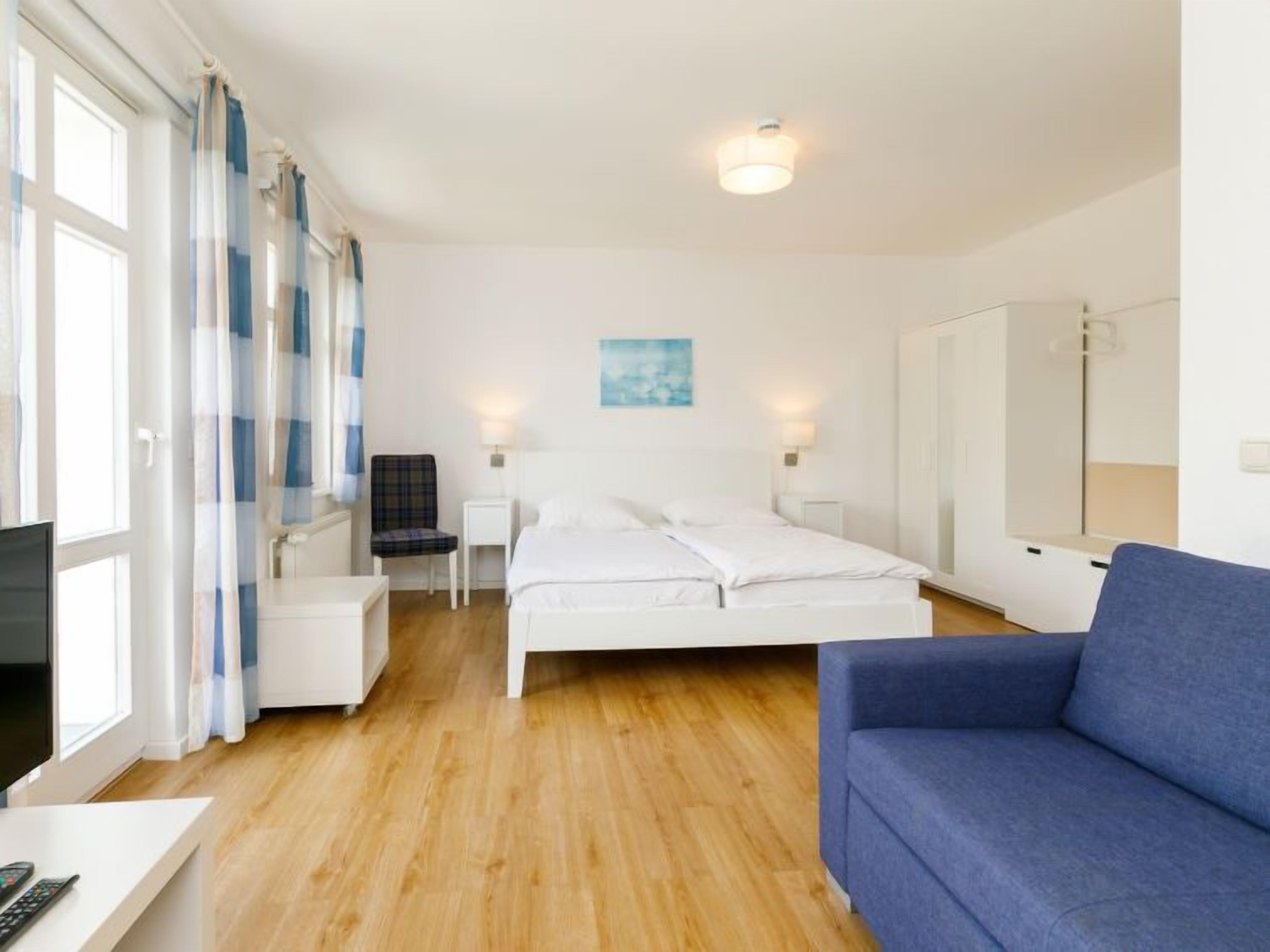 Une chambre d’hôtel avec un lit, un canapé bleu, une chaise, un bureau avec une télévision et une fenêtre avec des rideaux.