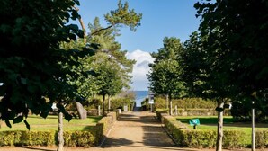 A paved pathway leading to a body of water, flanked by trees and hedges. - App.17 Zinnowitzer Hof by Interhome (Zinnowitz)