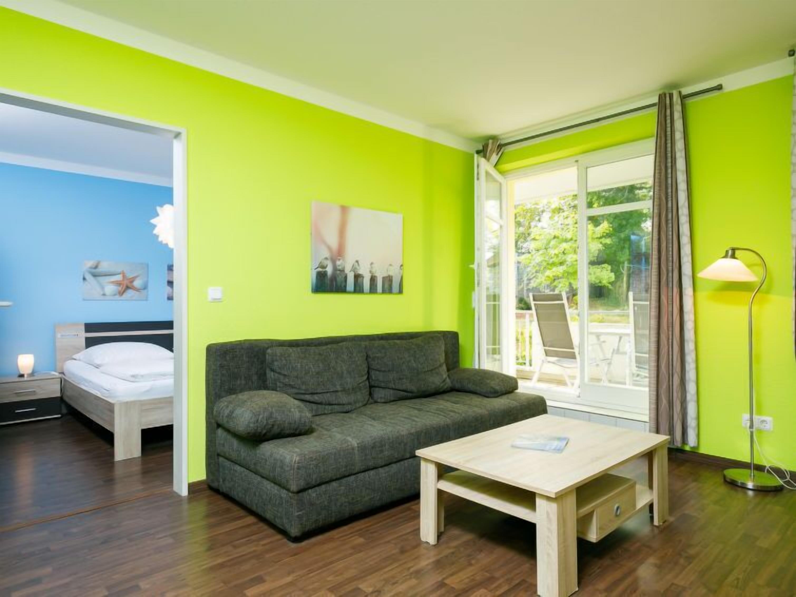 Una habitación con un sofá gris, una mesa de centro de madera, una cama con ropa de cama blanca y un cuadro en la pared.