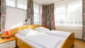 Un letto matrimoniale con lenzuola bianche, una testata in legno e un comodino con una lampada rossa.
