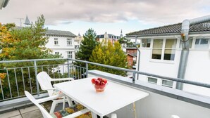 Un balcone con un tavolo bianco e due sedie bianche, una delle quali con un cuscino colorato.