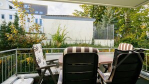 Un balcon avec une table et des chaises, entouré de verdure et d’immeubles.