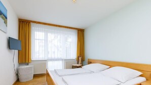 Une chambre d’hôtel avec un lit en bois, un téléviseur fixé au mur et une fenêtre avec des rideaux jaunes.