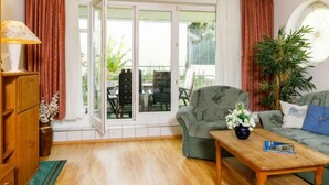 Un salon comprenant un canapé, une table basse et une lampe. Une porte-fenêtre coulissante donne accès à un espace extérieur aménagé avec des chaises et une table.
