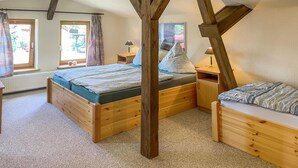 Ein gemütliches Schlafzimmer mit schrägverlaufender Decke, Holzbettgestellen und Blick ins Freie durch große Fenster.