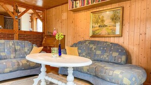 Ein gemütliches Zimmer mit Holzvertäfelung, einem runden weißen Tisch mit Blumenvase, zwei gemusterten Sofas und einem Gemälde an der Wand.