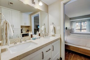 A modern bathroom with a double sink, a large mirror, and a wooden bed in the adjacent room. - Shadow Ridge 301 | Walk to Lifts | Mountain & Ski Views | Kitchen | Fireplace | Pool & Hot Tub (Park City)