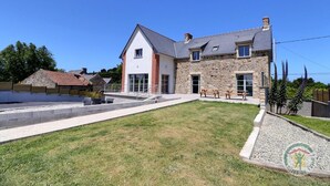 A two-story house with a stone facade, a large front lawn, and a patio area with outdoor seating.