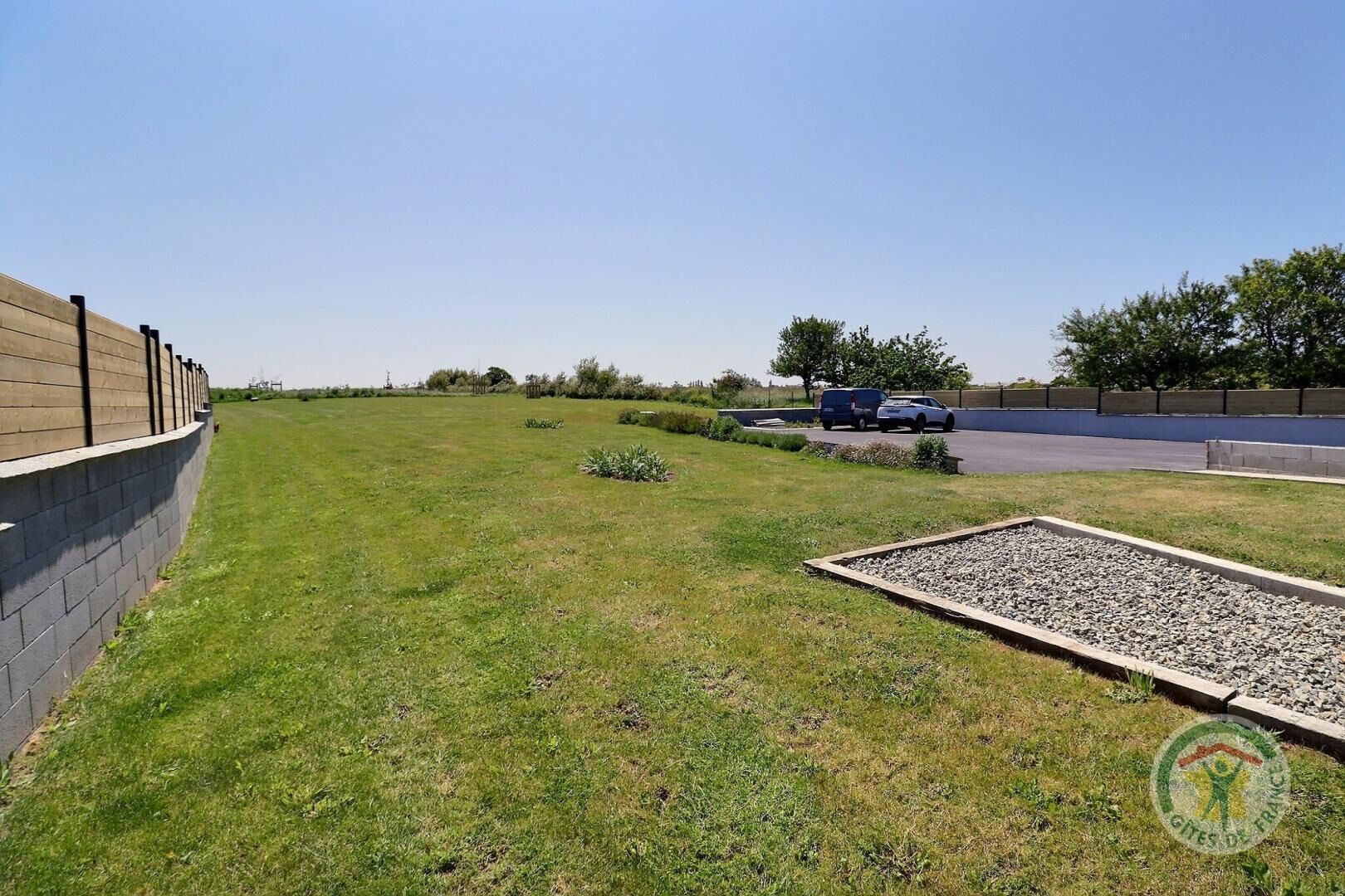 A grassy area with a paved path, a small garden bed, and a building with a brick wall.