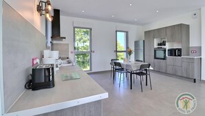 A modern kitchen with a dining area, featuring a large window, built-in appliances, and a minimalist design.