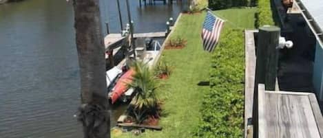 A view of a waterfront property with a dock, a grassy area with an American flag, and a wooden deck.