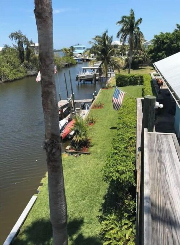 A view of a waterfront property with a dock, a grassy area with an American flag, and a wooden deck.