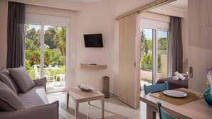 A modern hotel room with a sofa, a dining table, a TV, and a sliding glass door leading to an outdoor area. - Mear Luxury Apartments and Studios (Kantanos-Selino)