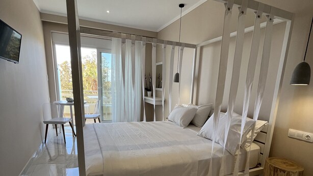 A modern bedroom with a large bed, a wooden side table, a small round stool, and a TV on the wall. - Mear Luxury Apartments and Studios (Kantanos-Selino)