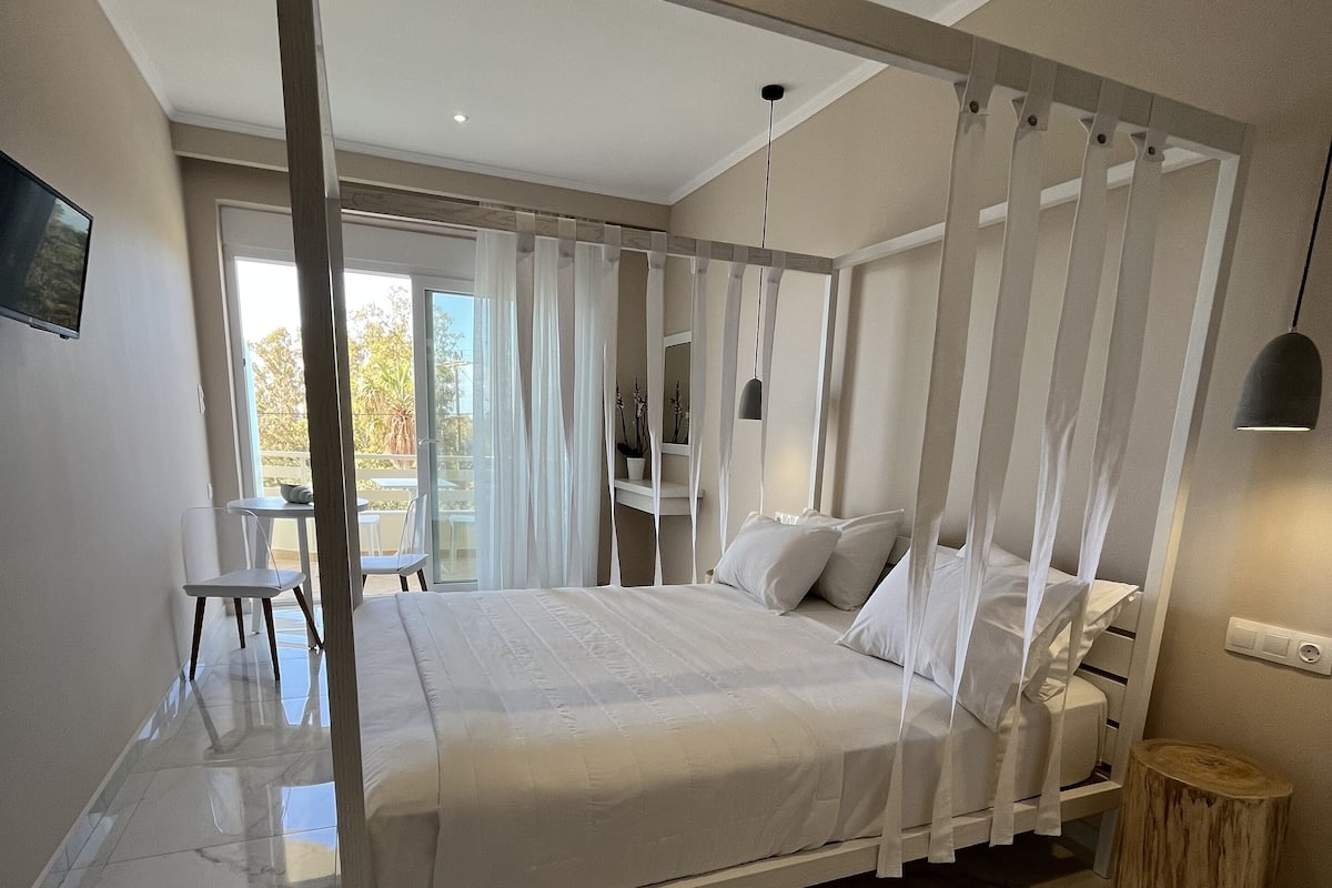 Ein modernes Schlafzimmer mit einem großen Bett, einem Holfnachtkästchen, einem kleinen runden Hocker und einem Fernseher an der Wand.
