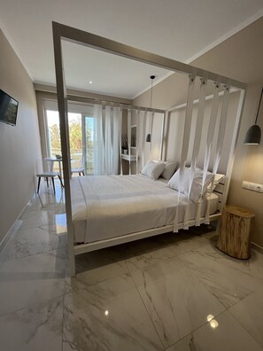 Un dormitorio moderno con una cama grande, una mesita de noche de madera, un taburete pequeño y redondo, y un televisor en la pared.