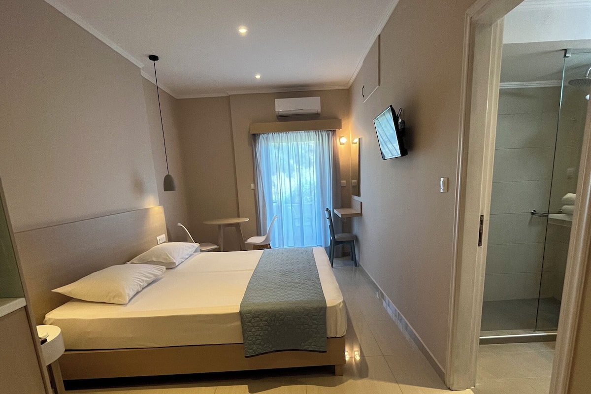 Ein Hotelzimmer mit einem großen Bett, einem Nachttisch, einem Sessel, einem an der Wand befestigten Fernseher und einer Duschkabine.