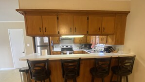 A kitchen with wooden cabinets, a white countertop, and four bar stools.