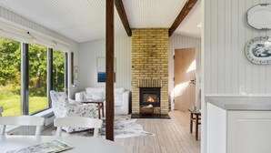 A cozy room with a fireplace, white furniture, and large windows overlooking a garden.