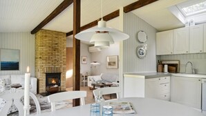 A cozy living room with a fireplace, a dining area with a white table, and a kitchen with white cabinets.