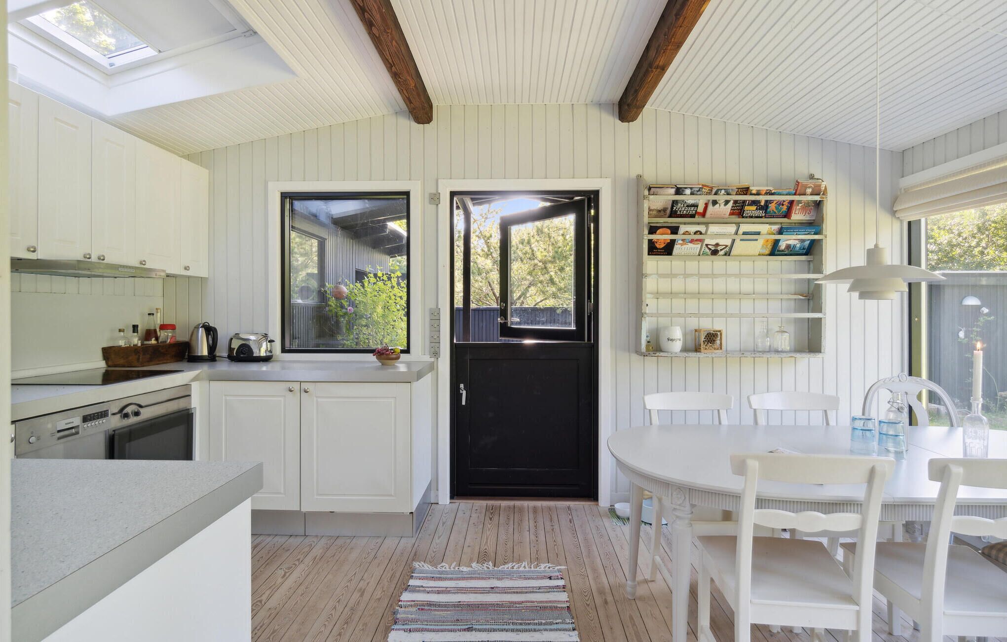 A compact kitchen with white cabinetry, a black door, and a window overlooking a garden.