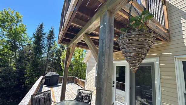 A wooden deck with outdoor furniture, a hanging basket, and a view of a forested area.