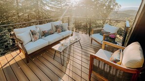 Eine Holzterrasse mit einem weißen Sofa, einem Korbsessel und einem kleinen Tisch mit Kerzen.