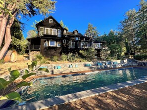 Une grande maison avec une piscine, entourée d’arbres et d’un mur de pierre.