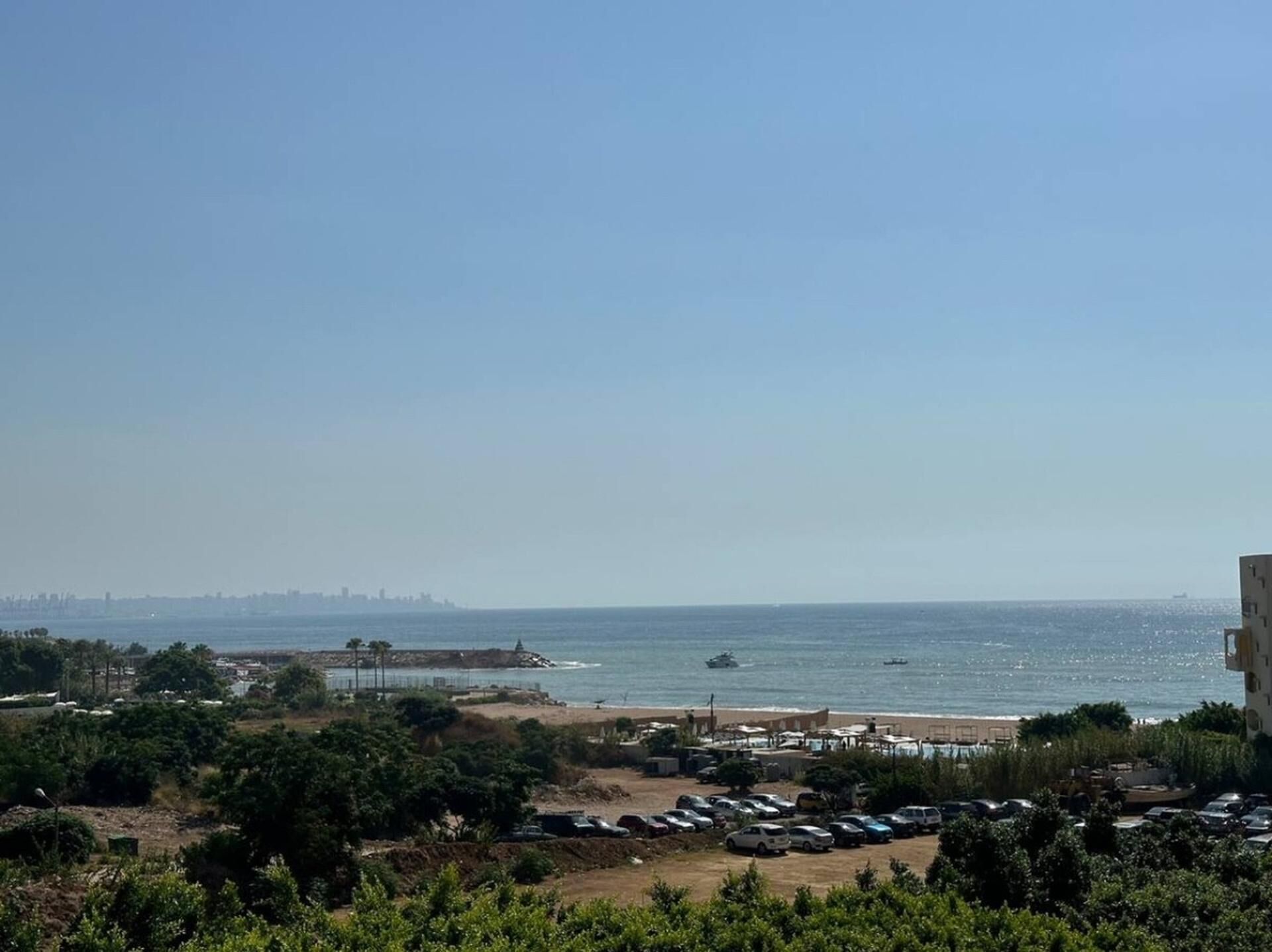 Blick auf die Küste mit Parkplatz, Strand und weiter Ferne der Stadtlandschaft.