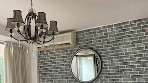 A living room with a brick wall, a round mirror, a beige sofa, a coffee table with a plant, and a chandelier. - Duplex in Siwar, 1 Bedroom, Next to Rimal, Wifi (Ghazir)