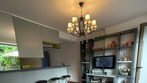 A modern living room with a sofa, a coffee table, and a TV. There are two bar stools and a bookshelf with decorative items. - Duplex in Siwar, 1 Bedroom, Next to Rimal, Wifi (Ghazir)