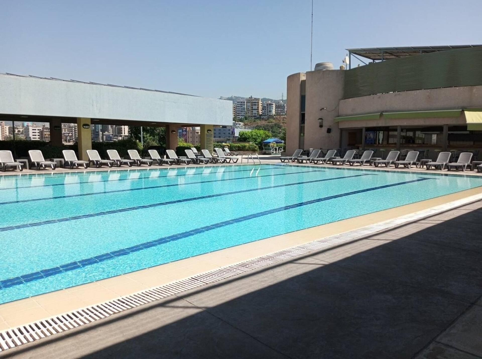 A swimming pool with multiple lanes, surrounded by lounge chairs and a covered area.