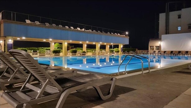 A swimming pool with lounge chairs, a covered seating area, and a building in the background. - Duplex in Siwar, 1 Bedroom, Next to Rimal, Wifi (Ghazir)