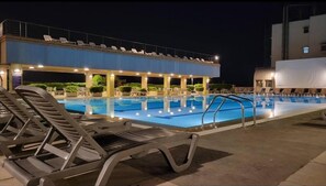 Une piscine avec des chaises longues, un espace de détente couvert et un bâtiment en arrière-plan.