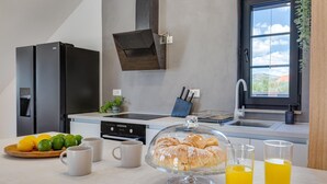 Een moderne keuken met een inbouwoven, een spoelbak en een raam met uitzicht op de omgeving. Er staan fruit, een glas sinaasappelsap en een bord croissants op het aanrecht.