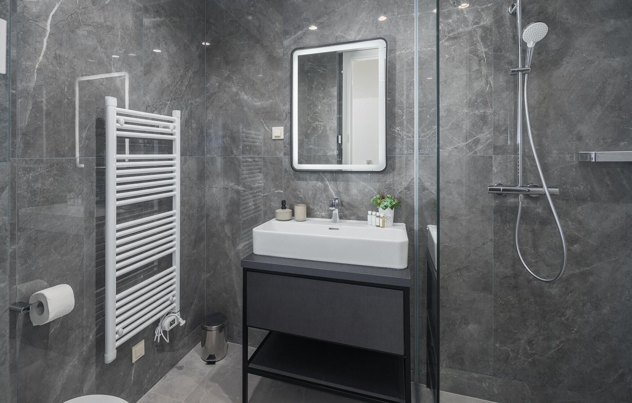 A modern bathroom with a glass-enclosed shower, a white sink with a mirror above it, and a towel rack with a white towel.