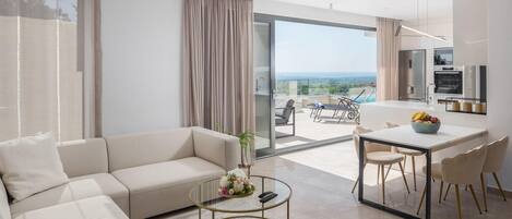 A modern living room with a sofa, coffee table, and dining area. A sliding glass door leads to a balcony with a view.