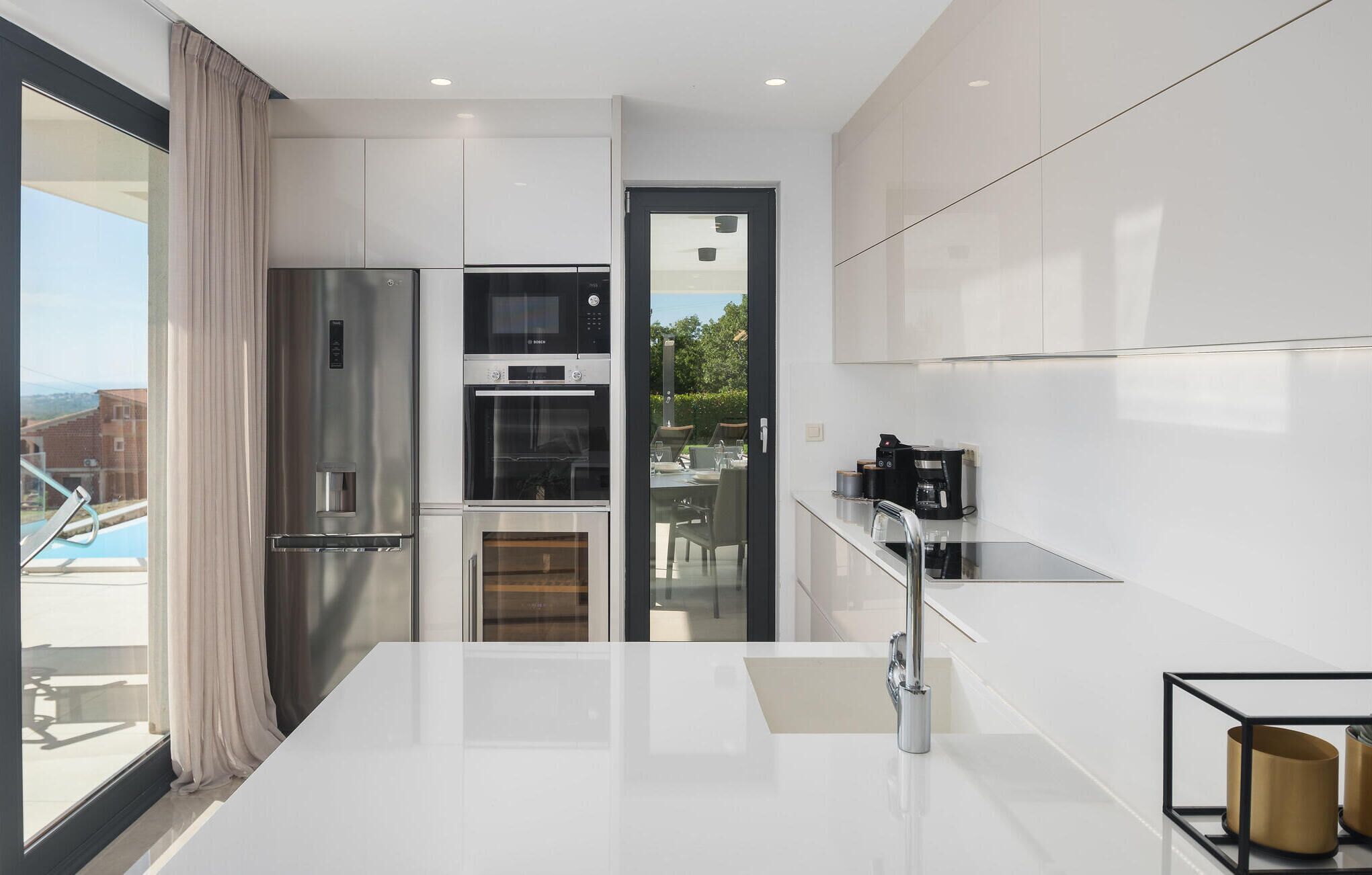 Een moderne keuken met roestvrijstalen apparatuur, een glazen deur naar een buitenruimte en een strak, minimalistisch design.