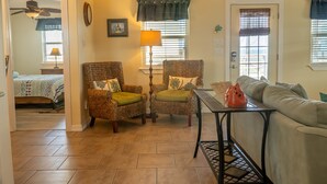 A living room with a sofa, two wicker chairs with green cushions, a table, and a ceiling fan.